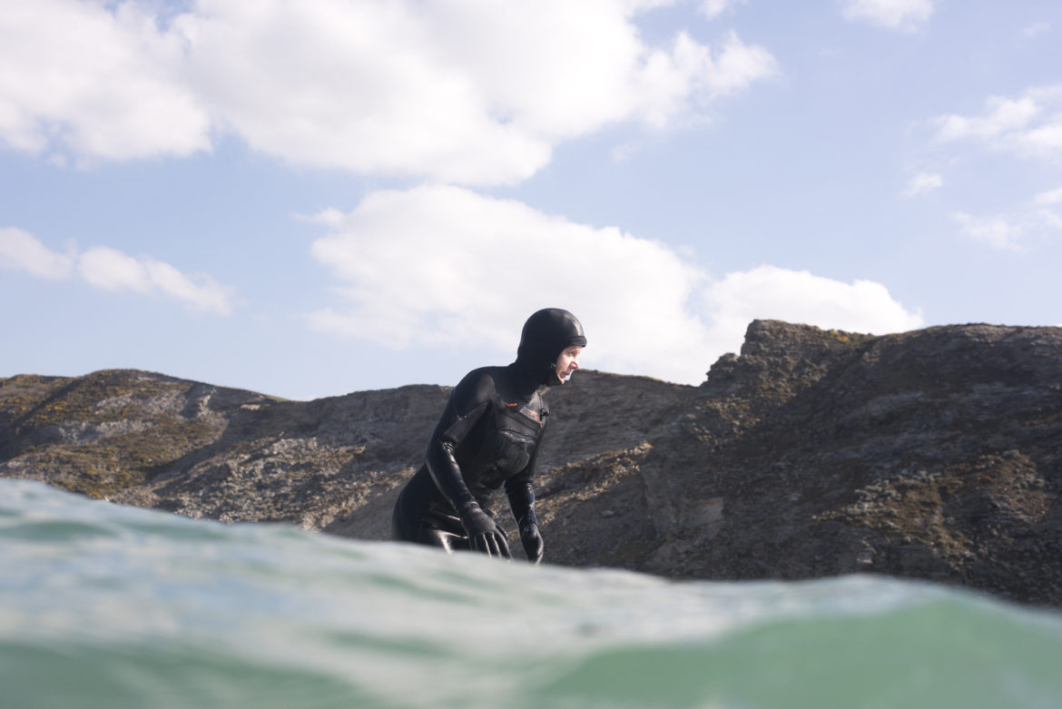 Female surfer glides along a wave wearing a hooded winter wetsuit