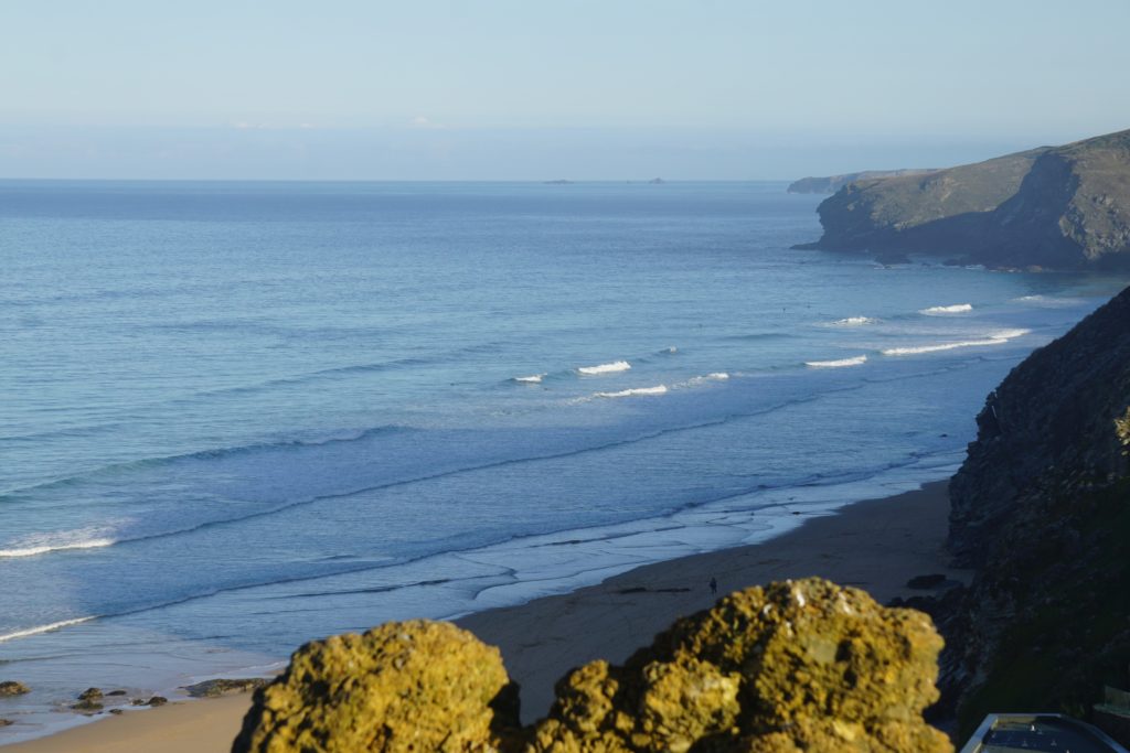 views of watergate bay and waves breaking with surfers out. 